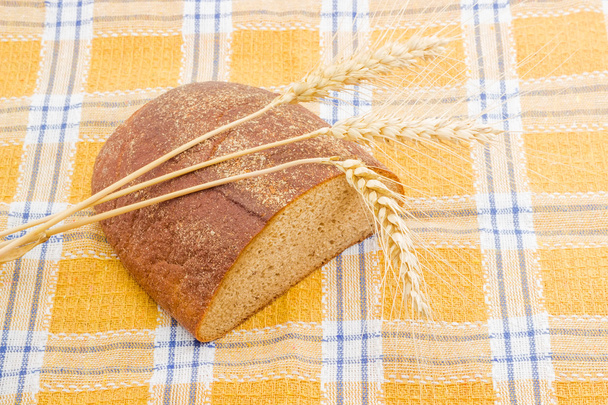 Brown bread and three spikes on a checkered tablecloth. - Photo, Image