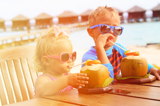 niño pequeño y niña bebiendo cóctel de coco en el resort de playa
 - Foto, Imagen