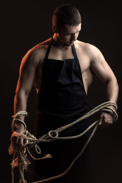 Muscular man in apron with rope - Фото, изображение