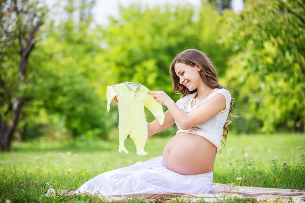 Mujer embarazada sosteniendo traje de bebé
 - Foto, Imagen