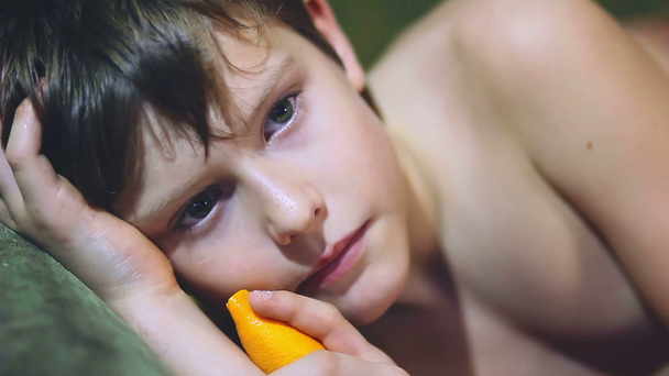 adolescente chico acostado de lado celebración lamido naranja cáscara
 - Imágenes, Vídeo