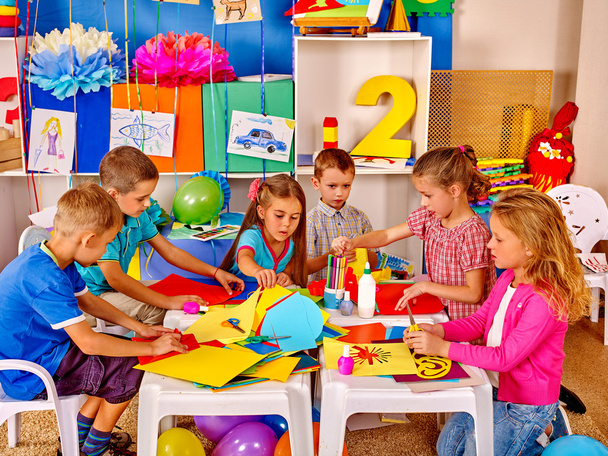 Kids holding colored paper and glue on table in kindergarten . - Photo, Image