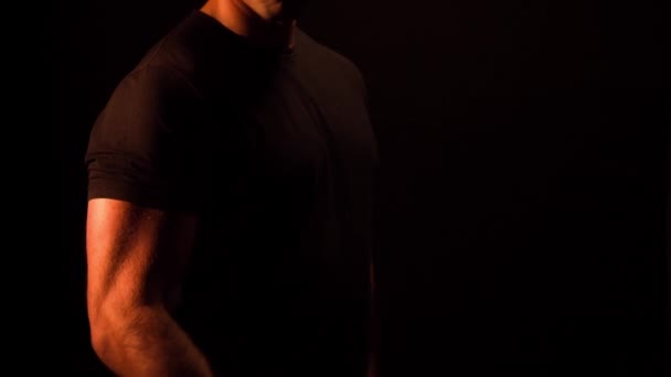 Muscular bodybuilder doing dumbbell curls on a black background - Video, Çekim