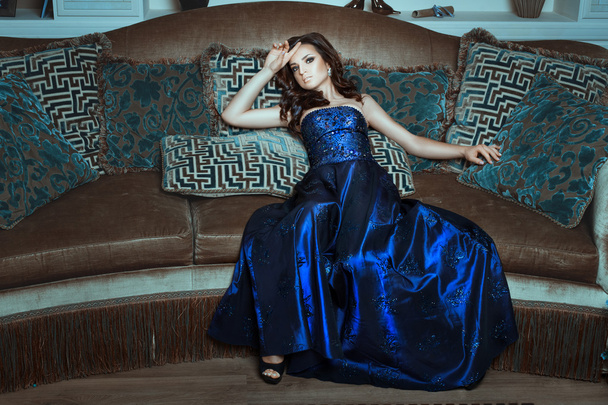 Dívka v modré a lesklé šaty pózuje prolhaný gauč. - Fotografie, Obrázek