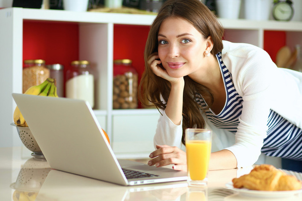atrakcyjna młoda kobieta za pomocą laptopa i siedzi w kuchni - Zdjęcie, obraz