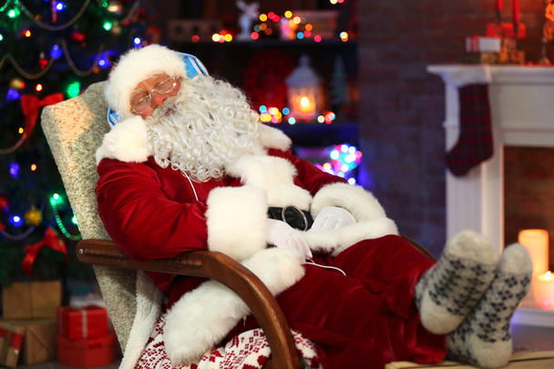 Santa Claus sitting with headphones sitting in comfortable rocking chair at home - Foto, Bild
