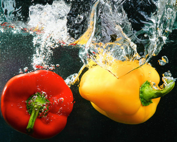 red and yellow peppers in water, isolated on black background - Photo, Image