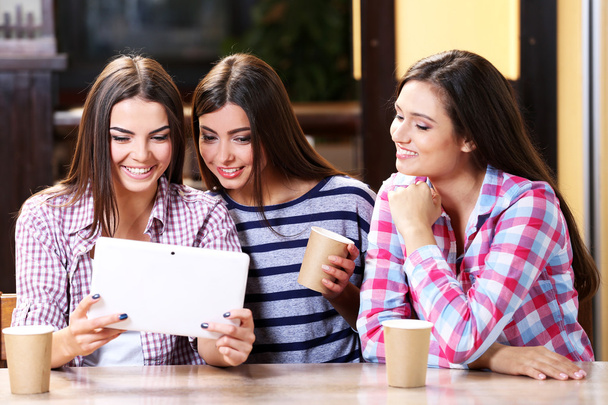 Three smiling friends with coffee looking at tablet - Foto, Imagem