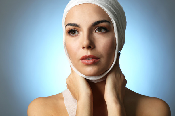 Young beautiful woman with a gauze bandage on her head, on grey-blue background - Foto, Imagem