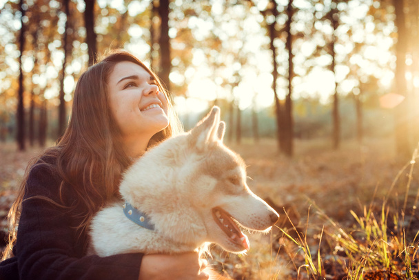 young happy female having fun with siberian husky dog in autumn park during sunset - Фото, зображення
