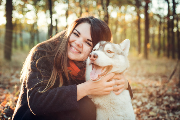 young happy female having fun with siberian husky dog in autumn park during sunset - Fotografie, Obrázek