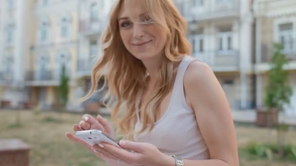 Młoda blond kobieta za pomocą jej telefon odkryty - Materiał filmowy, wideo