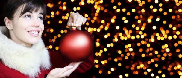 Christmas woman with red ball, smiling and looks up on lights ba - 写真・画像
