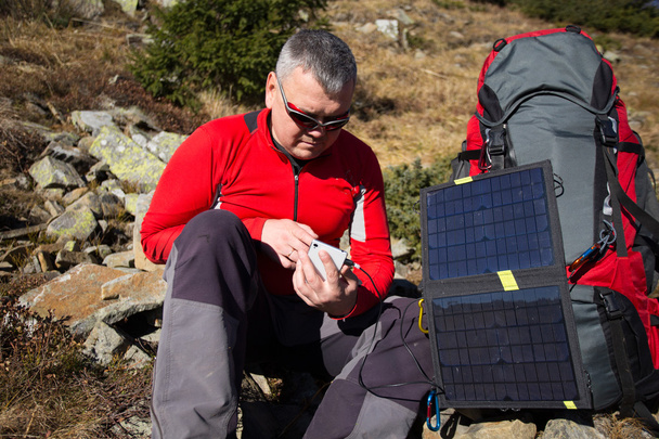 The solar panel attached to the tent. The man sitting next to mobile phone charges from the sun. - Valokuva, kuva