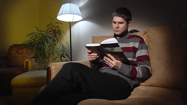 Le gars assis sur le canapé et lisant un livre
. - Séquence, vidéo