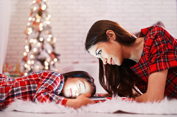 Mom and daughter are waiting for New Year presents near the Christmas tree. - 写真・画像