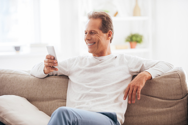 Cheerful mature man holding mobile phone - Foto, afbeelding