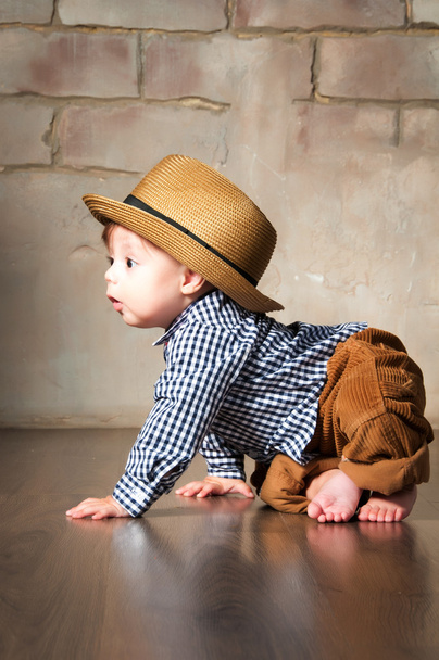 Llittle boy in retro hat and corduroy trousers learning to crawl on floor on all fours - 写真・画像