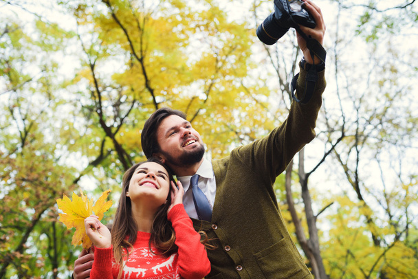 young happy couple making selfie using camera in autumn park - 写真・画像