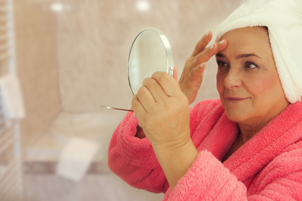 Portrait of an attractive middle aged woman looking into a mirror in the bathroom - Foto, immagini