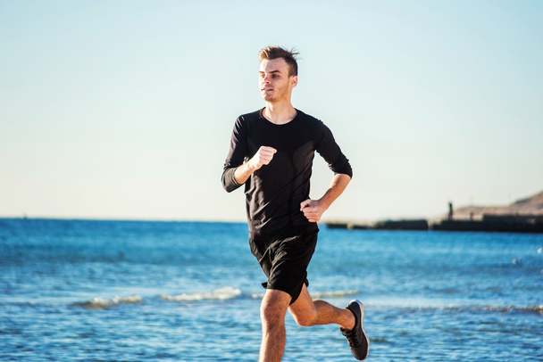 Running man. Male runner jogging during the sunrise on beach - Photo, Image