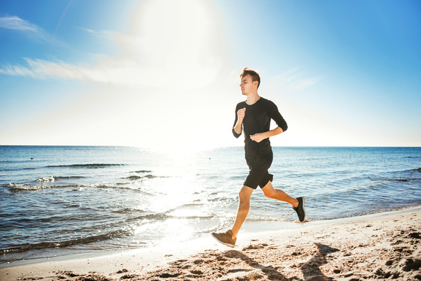 Running man. Male runner jogging during the sunrise on beach - Фото, изображение