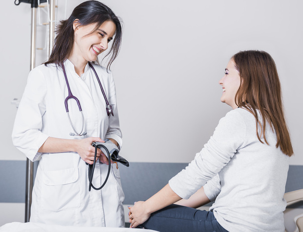 bela menina médico em um casaco branco verifica a pressão arterial na menina na cama
 - Foto, Imagem