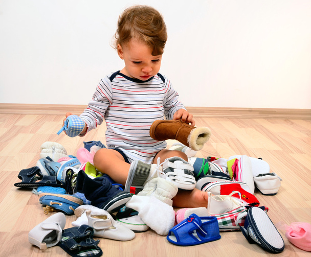 Toddler playing with a lot of baby shoes. - Photo, image