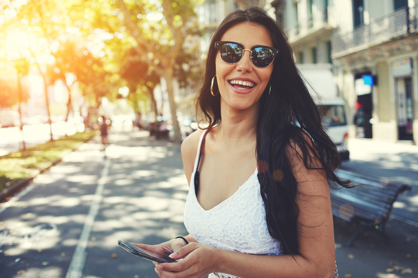 Latin woman in sunglasses using smartphone - 写真・画像