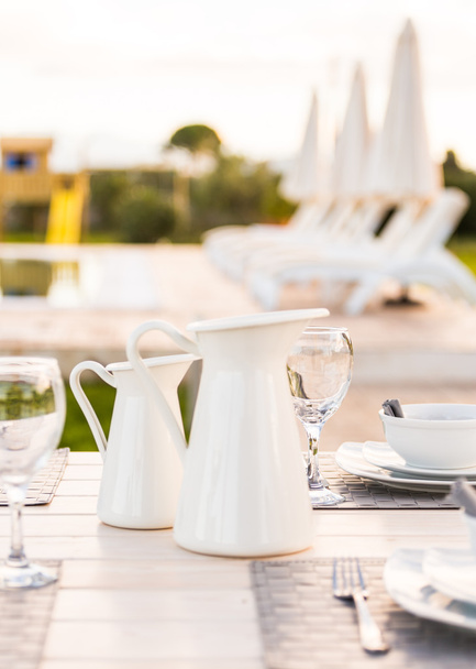 Elegantes jarras de vajilla blanca, cuencos, platos y copa de vino colocados en la mesa
 - Foto, Imagen