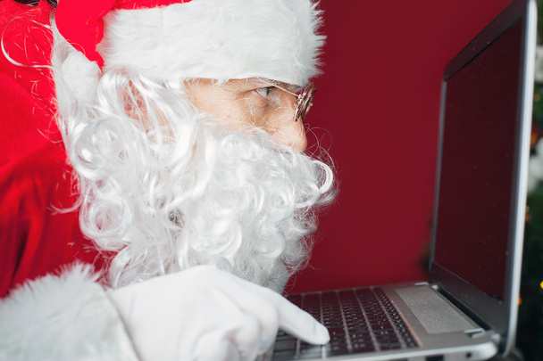 Santa Claus using laptop computer, looking at screen - Photo, image