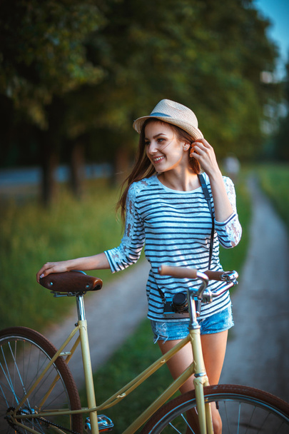 公園内の自転車と帽子の素敵な若い女性 - 写真・画像