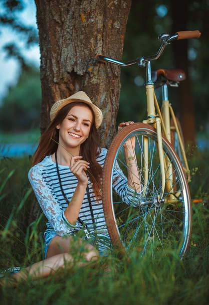 Lovely young woman in a hat with a bicycle in a park - Fotografie, Obrázek