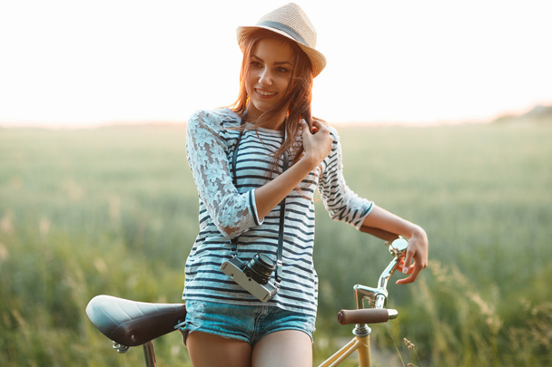 Schöne junge Frau steht mit ihrem Fahrrad auf einem Feld - Foto, Bild