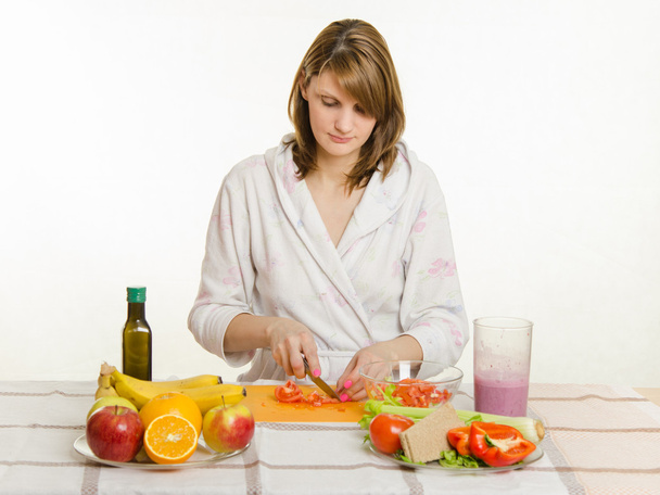 glückliche Hausfrau sitzt am Tisch und schneidet den Tomatensalat - Foto, Bild