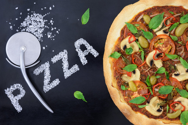 Pizza with cutter and salt  fun design on black baking tray. - Фото, зображення