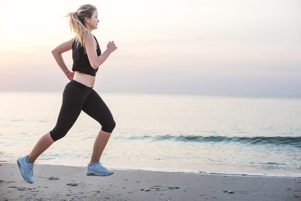 Laufende Frau. Läuferin joggt während des Sonnenaufgangs am Strand. - Foto, Bild