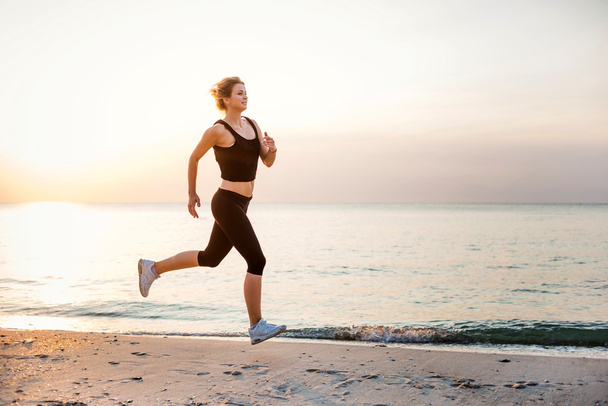 Running woman. Female runner jogging during the sunrise on beach. - Foto, imagen