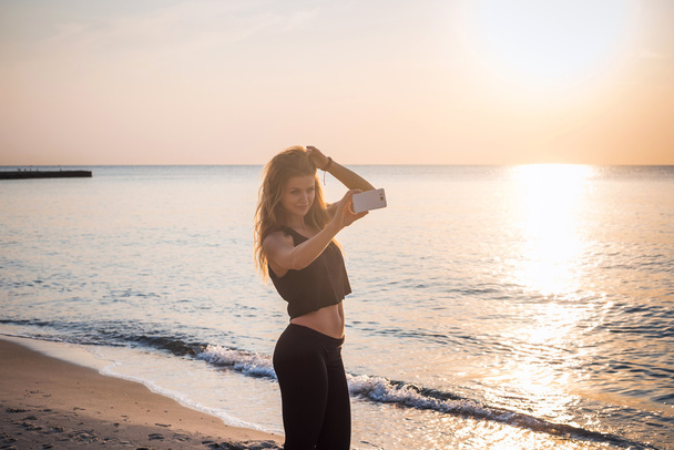 jeune beau modèle de fitness caucasien prendre des photos d'elle-même avec appareil photo de téléphone mobile sur la plage
 - Photo, image