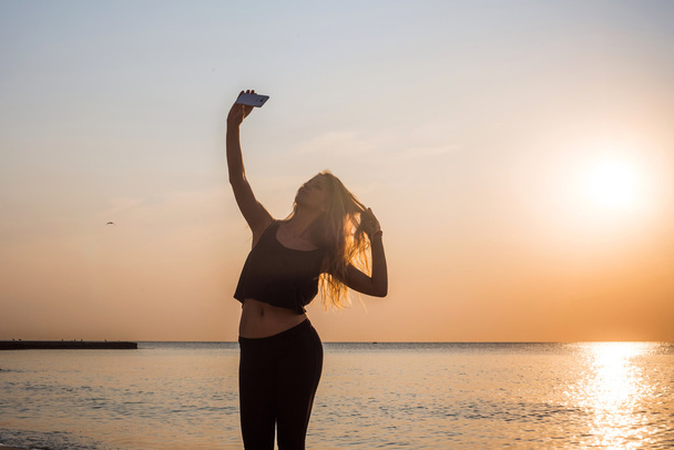 nuori kaunis valkoihoinen kunto malli ottaa kuvia itsestään matkapuhelimen kameralla rannalla
 - Valokuva, kuva