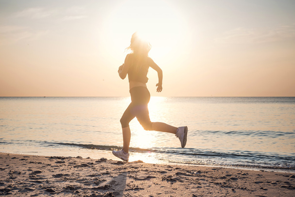 Systemem kobieta. Kobiece kobieta lekkoatletka joggingu podczas słońca na plaży. - Zdjęcie, obraz