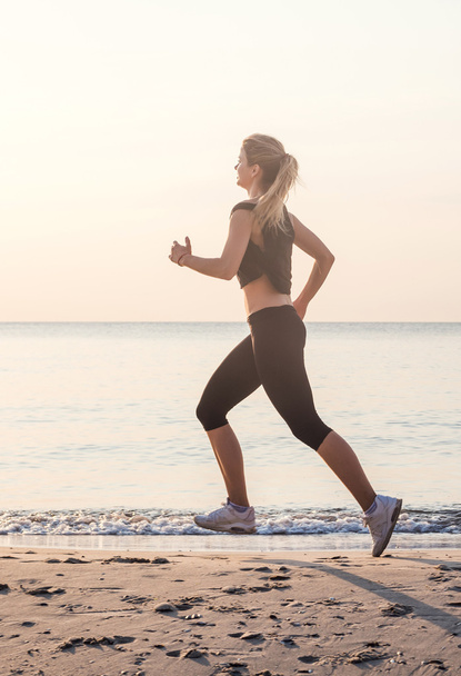 Running woman. Female runner jogging during the sunrise on beach. - Foto, afbeelding