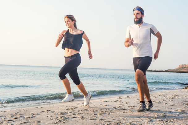 Running people - woman and man athlete runners jogging on beach. Fit young fitness couple exercising healthy lifestyle outdoors during sunrise or sunset - Foto, Imagem