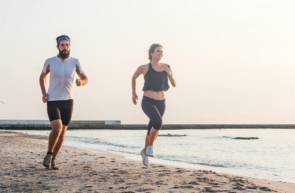 Systemem ludzi - kobieta i mężczyzna sportowiec biegaczy jogging na plaży. Zmieścić kilka młodych fitness ćwiczenia zdrowego stylu życia na zewnątrz podczas Wschodu lub zachodu słońca - Zdjęcie, obraz