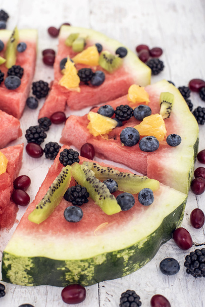colorful tropical fruit watermelon pizza topped with kiwifruit, blueberries, orange and fresh berries cut into segments on a rustic wooden board - Foto, Imagen