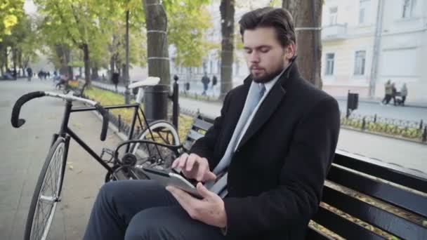 businessman using a tablet sitting on a bench near the bicycle - Кадри, відео