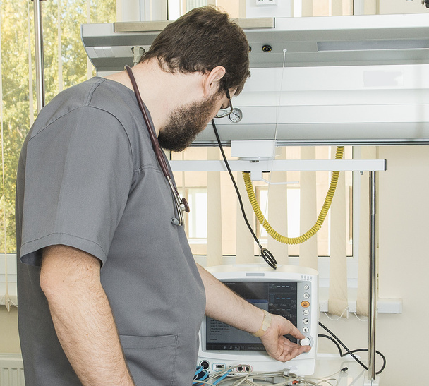 médico barbudo usando óculos e um manto cinza funciona com equipamento hospitalar
 - Foto, Imagem