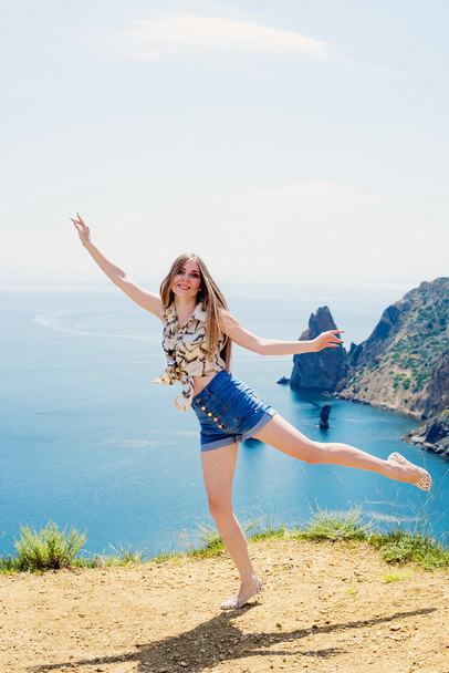 young caucasian female on a cliff above the sea enjoying the sun and freedom - Foto, Imagen