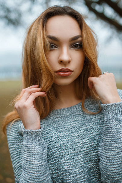 Close-up portrait of a beautiful young girl in stylish winter sweater on the background of a tree with fog - Photo, image