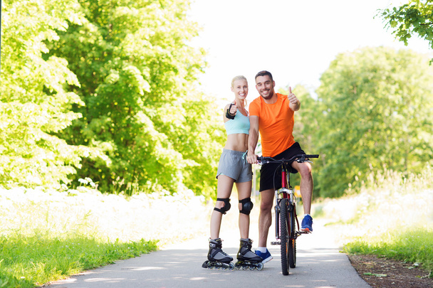 couple on rollerblades and bike showing thumbs up - Photo, Image